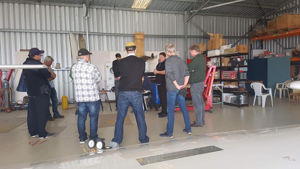 cameron leading a pilot course in a hangar with a group watching on